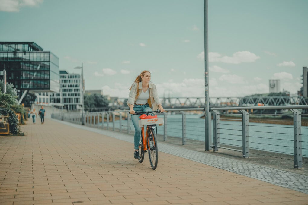 FWoman cycling along the Weser on a red John & Will bicycle, showcasing sustainable mobility and city exploration starting directly from the hotel.