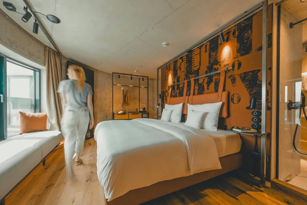 Spacious 24-square-meter Grode Stuuv with bed and window bench – woman passing by in a relaxed hotel moment at John & Will Bremen