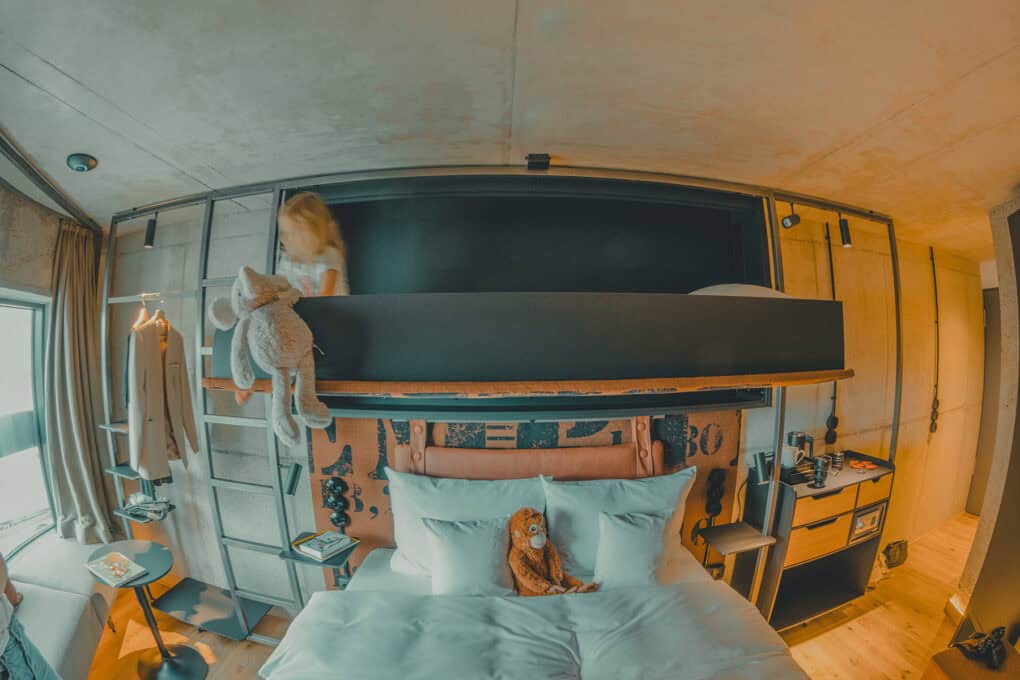 Lütt Stuuv – cozy two-person room with fold-out crib. Close-up of the bed with a child lying in the folded-out crib, warm and inviting atmosphere at the John & Will Hotel.