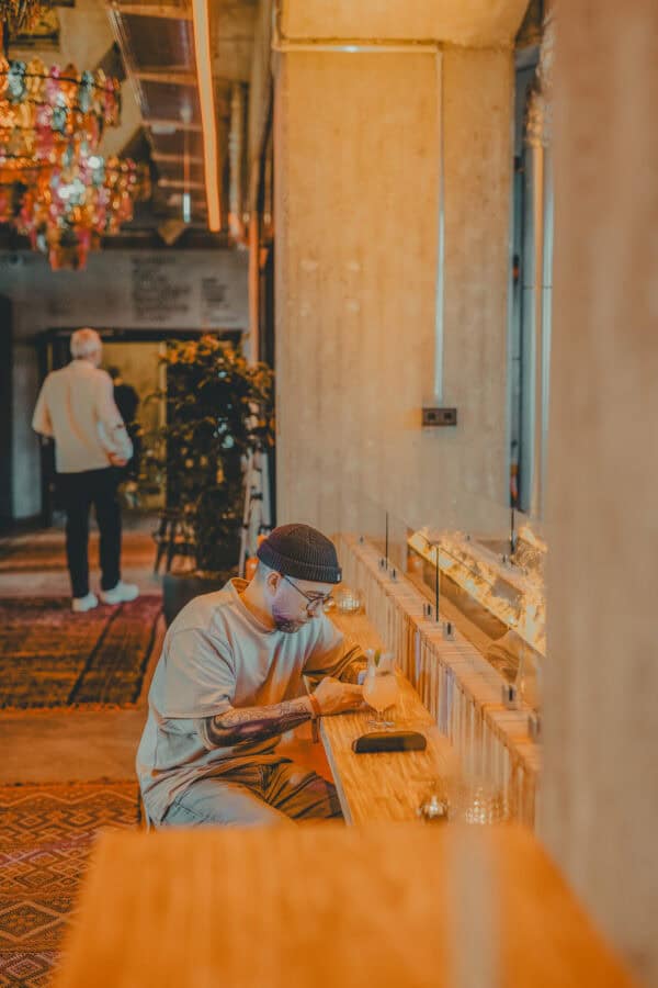 Person relaxing with a drink and smartphone in the Barception at John & Will hotel Bremen – casual 24/7 hangout spot