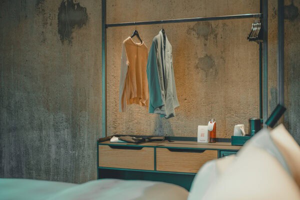 Hanging garments in a hotel room with exposed concrete wall and industrial steel structure – John & Will Bremen