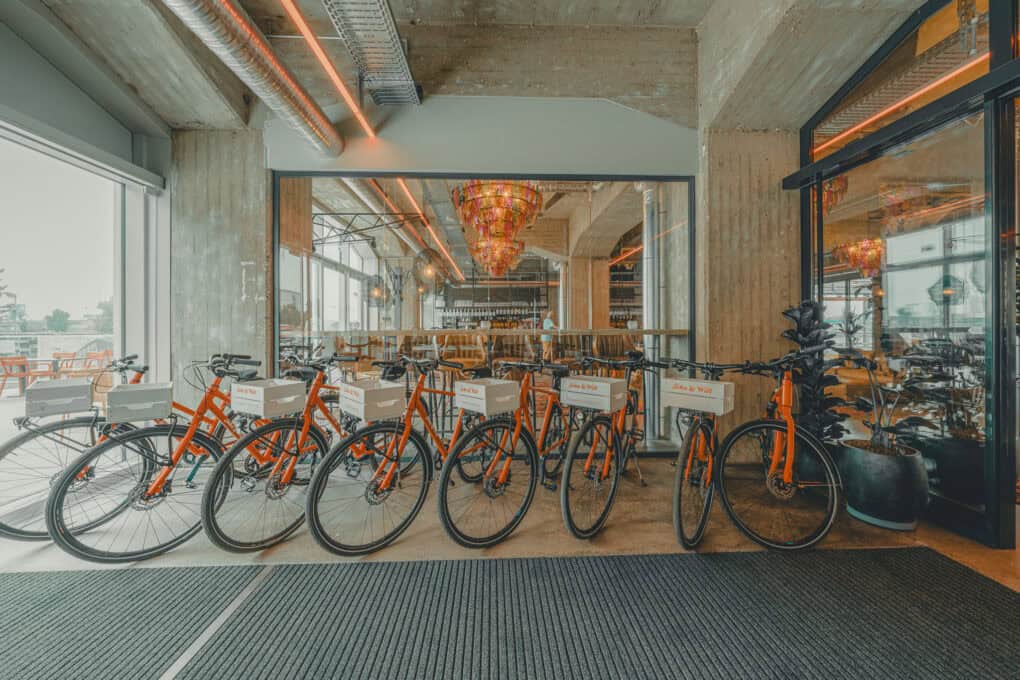 In the entrance area of John & Will, eight red rental bikes with transport boxes featuring the John & Will logo on the front handlebars.
