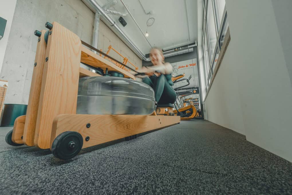 Fitness room at John & Will, photo of the water-powered rowing machine. In the blur, a person can be seen training on it.