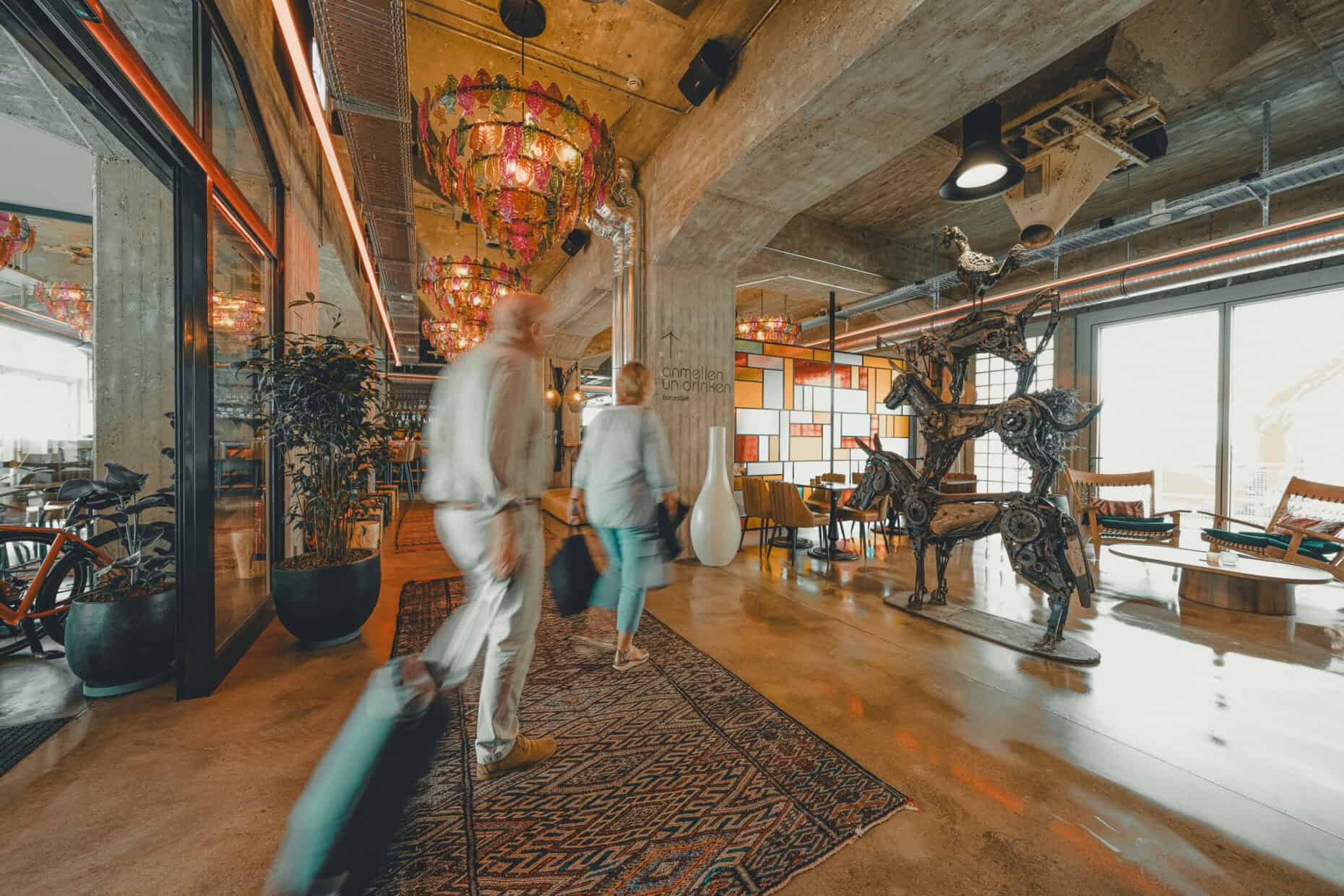 Two guests with luggage entering the John & Will lobby, passing by the art sculpture of the Bremen Town Musicians.