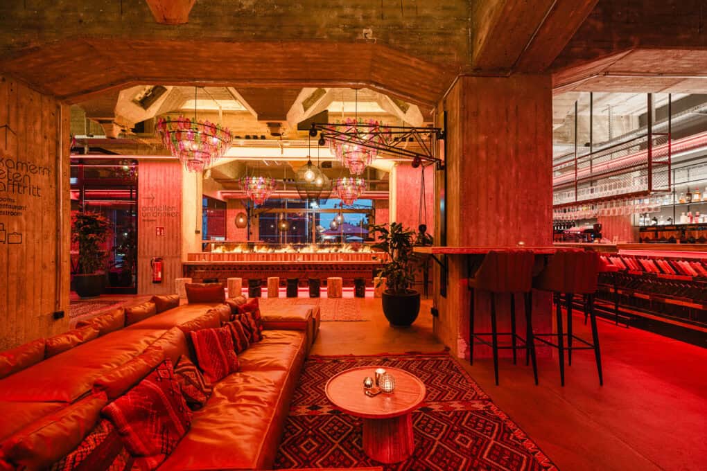 In rotes Licht gehüllte Barception mit gemütlicher Sitzlandschaft im John & Will Hotel Bremen – stilvolle 24/7 Bar mit nachhaltigem Design