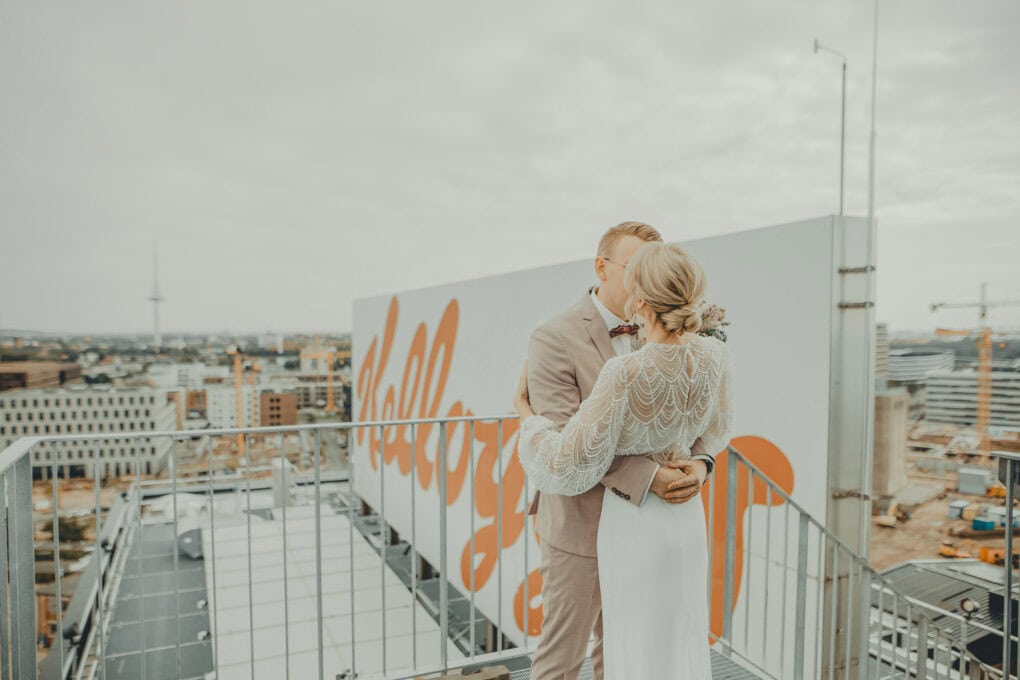 Hochzeitspaar küsst sich auf dem Dach des John & Will Hotels in Bremen vor dem ikonischen Kellogg-Schild – Hochzeit über den Dächern der Stadt