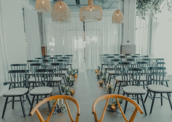 Hell und modern eingerichteter Veranstaltungsraum im John & Will Silohotel Bremen mit Reihen von schwarzen Stühlen, einem mit Kerzen und Pflanzen dekorierten Mittelgang und großen Fenstern mit weißen Vorhängen.