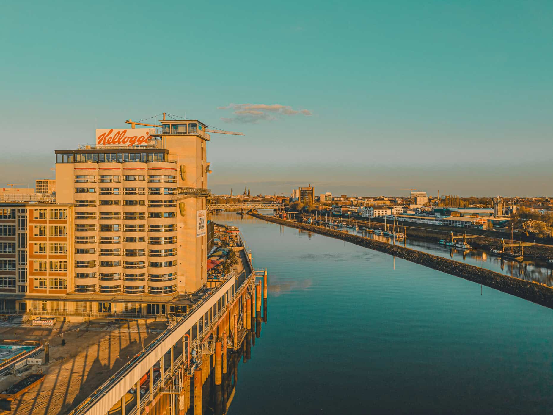 Panoramaaufnahme der ehemaligen Kellogg’s-Fabrik in der Bremer Überseestadt bei Sonnenuntergang – Blick entlang der Weser auf die Skyline der Stadt.